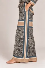 Palazzo de pierna ancha confeccionado en satén con estampado de animal print tipo cebra en tonos camel y negro, con detalles de bandas laterales y franja horizontal. Cuenta con cintura elástica fruncida y cordón ajustable.