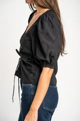 Blusa negra de algodón con diseño bordado sutil, escote en V y cordón ajustable fruncido en el centro del frente. Mangas cortas abullonadas.