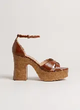 Sandalia de cuero color marrón, con tiras cruzadas en la parte delantera, plataforma y taco alto grueso forrado con textura símil madera, y tira ajustable al tobillo con hebilla metálica.