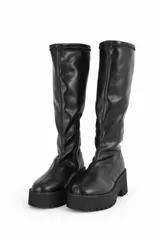 Bota de caña alta color negro, confeccionada en material sintético con acabado mate. Presenta una suela de plataforma track con taco cuadrado y cierre lateral interno.