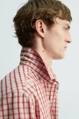 Camisa de algodón con cuello solapa, manga larga terminada en puño con botón y cierre frontal de botonadura. Presenta un patrón de cuadros en tonos rojo y beige.