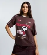 Remera de algodón color marrón con cuello redondo y mangas cortas. Presenta un estampado frontal con el personaje Snoopy en temática de carreras y detalles de líneas blancas contrastantes en los hombros y mangas.