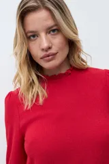 Blusa de color rojo con cuello alto y detalle de volados, mangas largas con puños elásticos en punto smock y textura sutil en la tela.