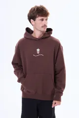 Buzo tipo canguro color marrón, de corte oversize, con capucha y bolsillo frontal tipo canguro. Presenta un pequeño estampado central con un vaso de café y una frase debajo.