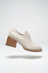 Zapato de cuero color beige, con taco de madera y suela dentada. Presenta un diseño slip-on con detalles de textura en relieve en los laterales y el empeine.
