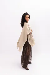 Ruana de tejido de punto en color arena, con diseño cruzado, escote en V y terminaciones con flecos en el ruedo. Incluye un parche de cuero con la marca Pura Lana en la parte frontal.