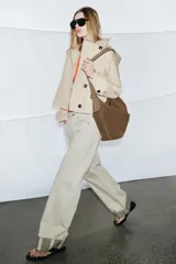 Trench corto color verde militar, con cuello solapa y capucha. Tiene manga larga con trabillas y botón en los puños, bolsillos delanteros y bajo asimétrico. Cierre frontal con botones. El tejido es repelente al agua.