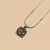 Collar de cadena trenzada en plata con detalles en oro, que incluye un dije circular de plata envejecida con el diseño de una flor de lis en relieve y detalles dorados en el borde.
