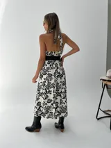 Vestido midi blanco con estampado floral negro, escote halter y cinturón ancho negro.