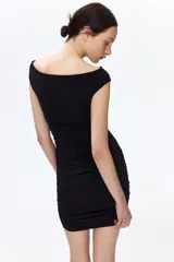 Vestido corto negro en punto texturizado, de corte entallado con hombros descubiertos, escote en V y frunces laterales que generan un efecto drapeado. Cuenta con un nudo ancho asimétrico al frente.