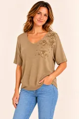 Remera de punto color marrón camel con escote en V y mangas cortas. Presenta aplicaciones de flores de tela y detalles de perlas y tachas doradas en el hombro y pecho.