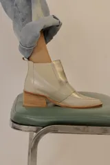 Botín de cuero color crema con puntera cuadrada, elástico lateral plateado y detalle de tira con textura reptil cruzada sobre el empeine.