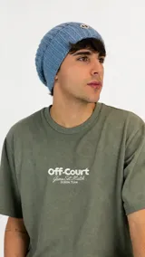 Gorro tipo beanie de punto grueso en color azul, con textura acanalada y parche circular con logo en la parte frontal.