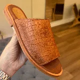 Sandalias tipo chata de cuero negro con textura de reptil, suela plana con borde en tono madera y plantilla acolchada.