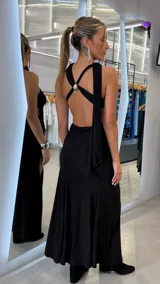 Vestido largo negro con brillo, diseño de un solo hombro con tiras cruzadas en la espalda y detalle de aplique metálico.