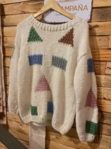Buzo de lana merino color marfil, tejido a mano con dos agujas, adornado con formas geométricas bordadas o tejidas en varios colores como verde, marrón, celeste y rosado.
