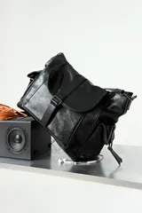 Cartera tipo hobo de cuero vegano color negro, con tapa frontal, cierre de hebilla y múltiples bolsillos laterales con cierre. Incluye dos correas, una corta fija y una regulable extraíble.