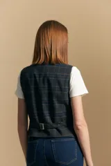 Chaleco sastrero de corte entallado con estampado de cuadros en tonos beige, marrón y azul. Presenta escote en V, cierre frontal con botones y terminación en punta en el ruedo. Incluye ajuste con hebilla en la espalda.