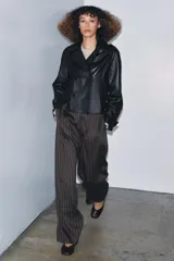 Cazadora corta de piel 100% negra, con cuello solapa de muescas, cierre frontal cruzado de doble botonadura, mangas largas ajustables con hebillas y bolsillos delanteros.