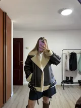 Campera tipo gamulán de cuero sintético en color marrón oscuro, con interior y solapas de corderito sintético en color crema. Presenta cierre frontal, bolsillos laterales con cierre, correas ajustables con hebillas en el cuello y en el ruedo, y puños con detalle de corderito.