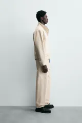 Cazadora de algodón color beige claro, corte relajado, con cuello subido y manga larga. Cierre frontal con cremallera oculta por solapa con cierres metálicos tipo alamar.