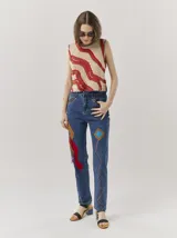 Pantalón de jean tiro alto tipo mom-fit, con parches de colores en forma geométrica, detalles de tientos de cuero trenzados en la cintura y adornos de canutillos en la parte frontal.