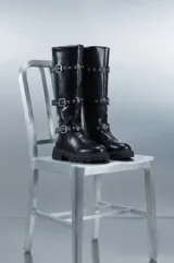 Botas bucaneras de cuero sintético negro, con suela track y tres tiras con hebillas metálicas y ojales decorativos alrededor de la caña alta.