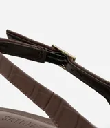 Tacones slingback Satinato en color marrón con textura crocco, puntera fina, taco bloque mediano y tira ajustable con hebilla en el talón.