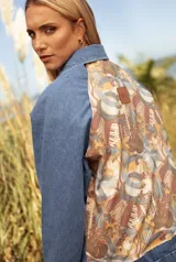 Campera de jean con mangas y frente en denim azul, y panel trasero estampado con motivos musicales y florales en tonos tierra. Incluye un parche de cuero con el logo de la marca en la parte superior de la espalda.