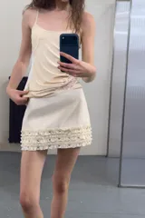 Falda mini de tiro medio en color crudo, con detalle de volantes en el ruedo adornados con tachas metálicas. Cuenta con cierre lateral oculto.