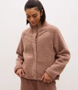 Campera bomber de mujer confeccionada en tejido sherpa color rosa viejo, con cuello alto, cierre frontal con cremallera y detalles de paneles lisos contrastantes en el pecho.