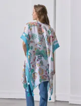 Kimono ligero de manga corta, color blanco, con estampado floral estilo cachemira en tonos pastel (naranja, verde menta, celeste). Presenta bordes y detalles en azul turquesa con borlas colgantes en el ruedo.