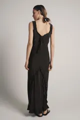Vestido largo de viscosa en color negro, con escote redondo y tirantes anchos con detalle de volados. Presenta bordados florales a tono en la parte superior y bajo con terminación evasé.