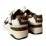 Championes urbanos de diseño robusto, combinando paneles de cuero y eco cuero en tonos marrón y blanco. Presentan cordones gruesos tipo soga, suela de plataforma con textura y detalles de marca grabados en el lateral.