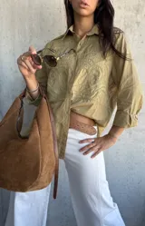 Camisa oversize de color verde oliva, con cuello clásico y cierre frontal de botones. Presenta un diseño bordado detallado en la parte superior delantera y mangas largas con puños.