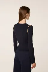 Sweater de punto fino color negro, con cuello redondo y mangas largas. Presenta un diseño ajustado con un corte asimétrico en el ruedo delantero y detalles de cuentas doradas en las costuras de los hombros.