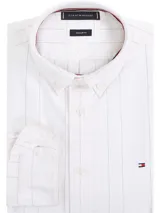 Camisa de hombre Tommy Hilfiger de corte regular, confeccionada en algodón Oxford blanco con finas rayas verticales en azul y rojo. Tiene cuello abotonado, puños redondeados con botón y logo bordado en el pecho.