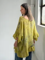 Blusa color verde pistacho, de corte holgado, manga corta con volados y diseño asimétrico con volado en el ruedo. Cuenta con un estampado floral difuminado en el frente.