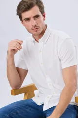 Camisa de manga corta confeccionada en tejido piqué de algodón, color blanco, con cuello con botones y cierre frontal abotonado.