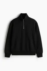 Buzo negro de corte holgado, confeccionado en tejido pesado de mezcla de algodón con interior cepillado. Cuenta con hombros caídos, cuello elevado con medio cierre metálico, y puños y bajo en punto acanalado.