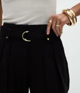 Pantalón de sastrería corte carrot, color negro, con pliegues delanteros, cintura alta y cinturón desmontable con hebilla metálica. Presenta un diseño holgado en las caderas que se estrecha hacia el ruedo con dobladillo estructurado.