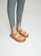 Sandalias de cuero vacuno color marrón con acabado brillante, diseño de dos tiras anchas acolchadas y plataforma baja.
