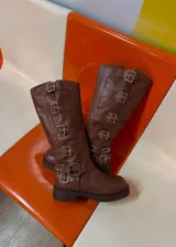 Bota alta estilo biker color marrón, con suela plana chunky y múltiples correas horizontales con hebillas metálicas plateadas en la caña y en el empeine.