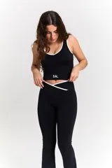 Conjunto deportivo compuesto por un top y un pantalón largo. El top es negro con ribetes blancos, escote redondo y logo 'bk.' estampado en el frente. El pantalón es negro, de corte acampanado, con cintura cruzada en V y detalle de ribete blanco.