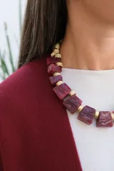 Collar de diseño llamativo compuesto por piezas geométricas de resina en tono rojizo veteado, intercaladas con separadores metálicos dorados de textura acanalada.