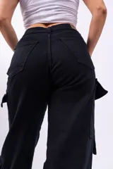 Pantalón cargo negro de jeans sin lycra, corte holgado y tiro alto. Cuenta con múltiples bolsillos laterales con solapa y cordones ajustables.