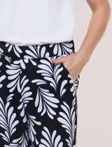 Pantalón crop de lino y rayón marca Dash, con estampado de hojas en blanco sobre fondo negro. Presenta tiro medio, pretina elástica en la parte trasera y bolsillos frontales.