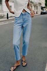 Jeans de tiro alto con diseño mom fit, tobilleros, de cinco bolsillos y cierre frontal con cremallera y botón, en color azul claro con efecto deslavado.