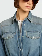 Vestido camisero largo de denim azul claro, con cuello camisero, botones frontales, bolsillos de parche en el pecho y mangas largas. Incluye un cinturón ancho de la misma tela anudado a la cintura.