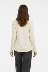 Remera blanca de manga larga, entallada, con cuello redondo y una hilera de botones en el frente. Incluye un pequeño bolsillo decorativo en el pecho.